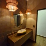 Mueble de baño contemporáneo con mesón en piedra sintetizada, veta tipo madera y espejo orgánico en Medellín